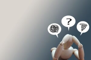 頭を抱える木製の人形と、もつれた線・疑問符・渦巻きの吹き出し